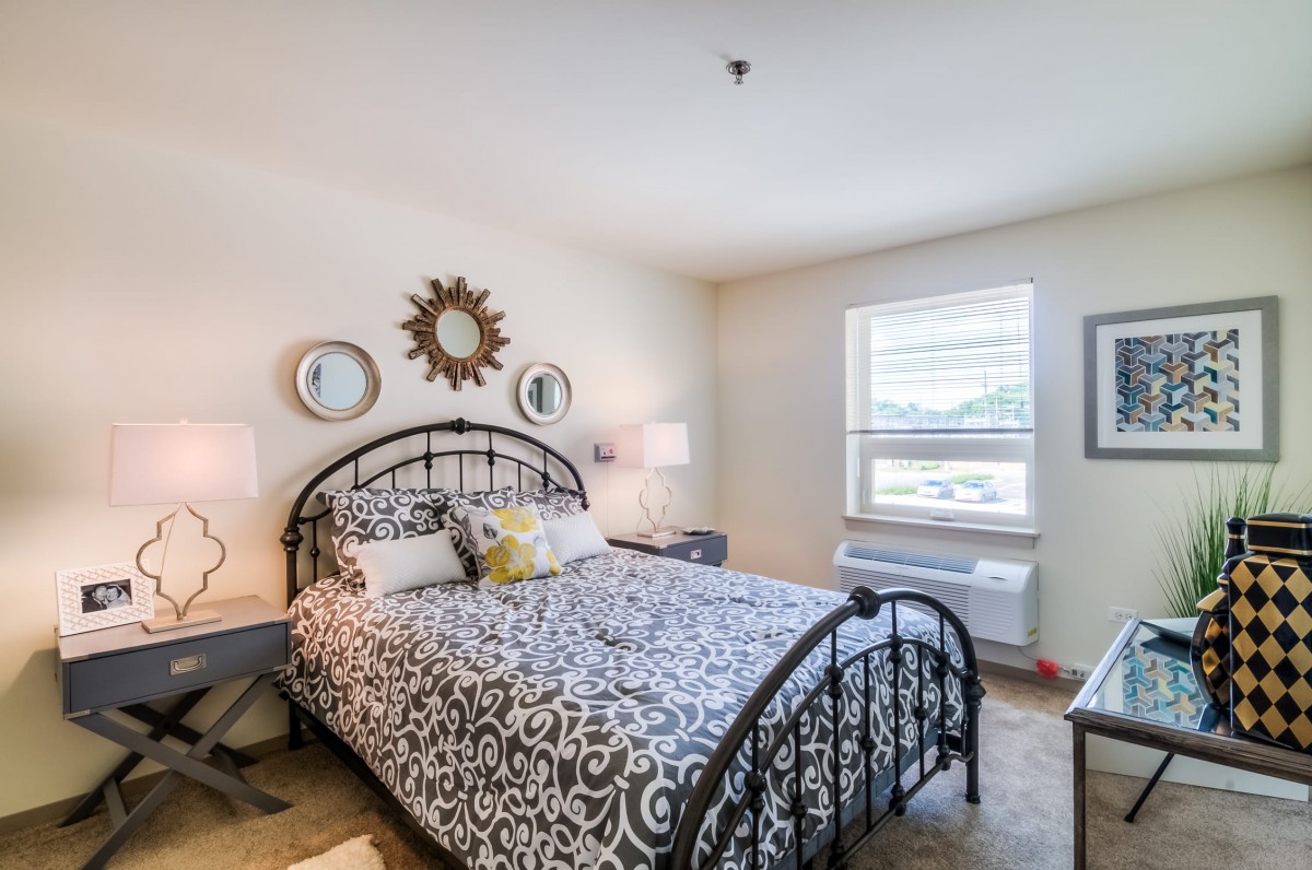 A cozy bedroom with a metal bed frame and patterned bedding, featuring decorative mirrors and bedside lamps.