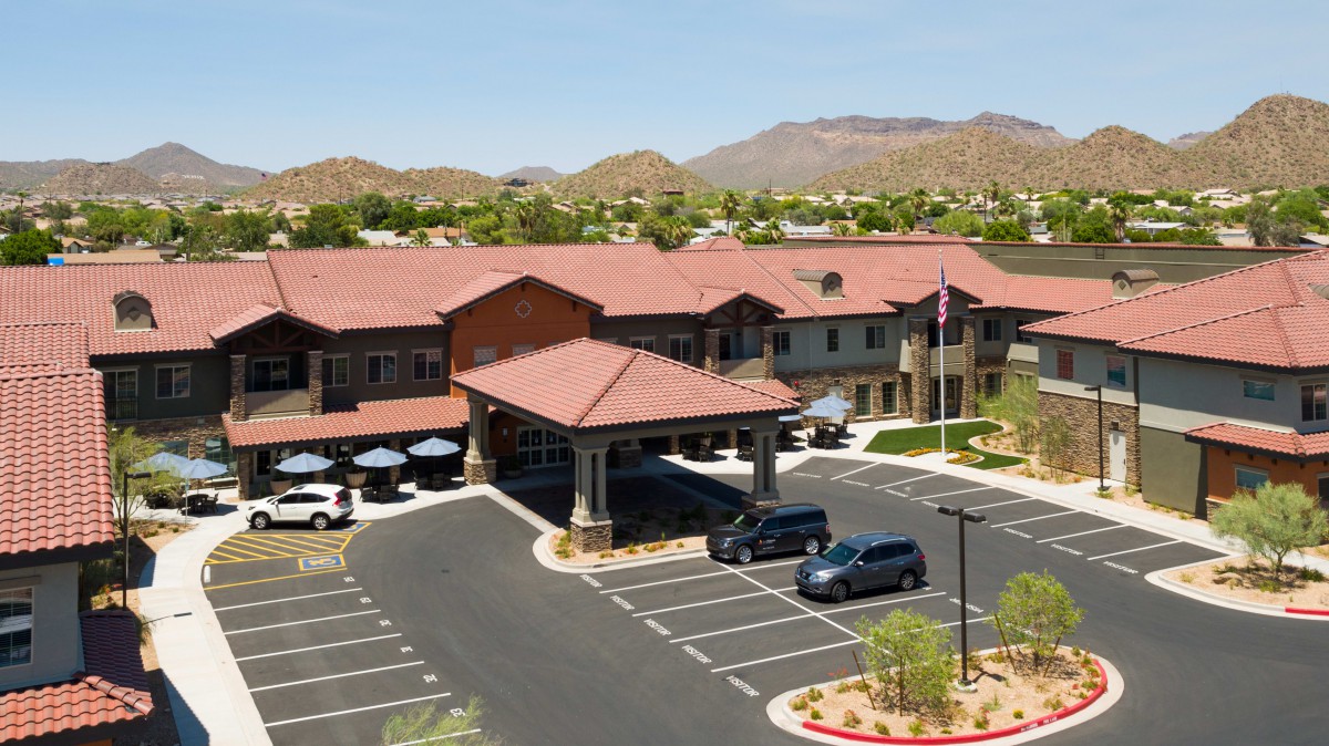 A large building with a parking lot surrounded by mountains and trees under a clear sky.