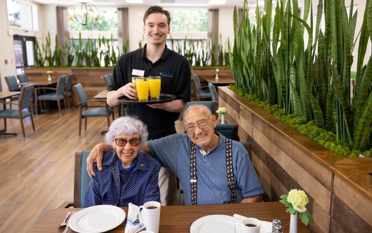 A cheerful elderly couple enjoying drinks with a friendly waiter at a restaurant.