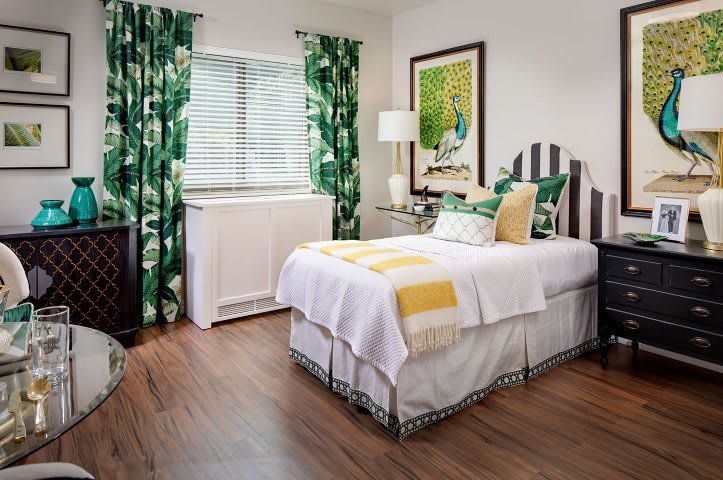 A cozy bedroom with colorful decor, featuring a single bed, patterned curtains, and framed artwork.