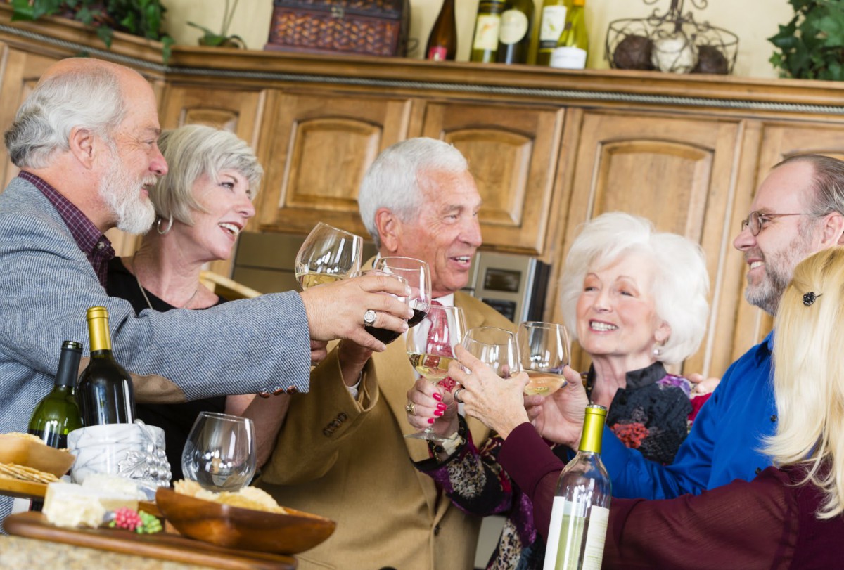 A group of elderly friends making a toast with wine glasses in a kitchen setting.