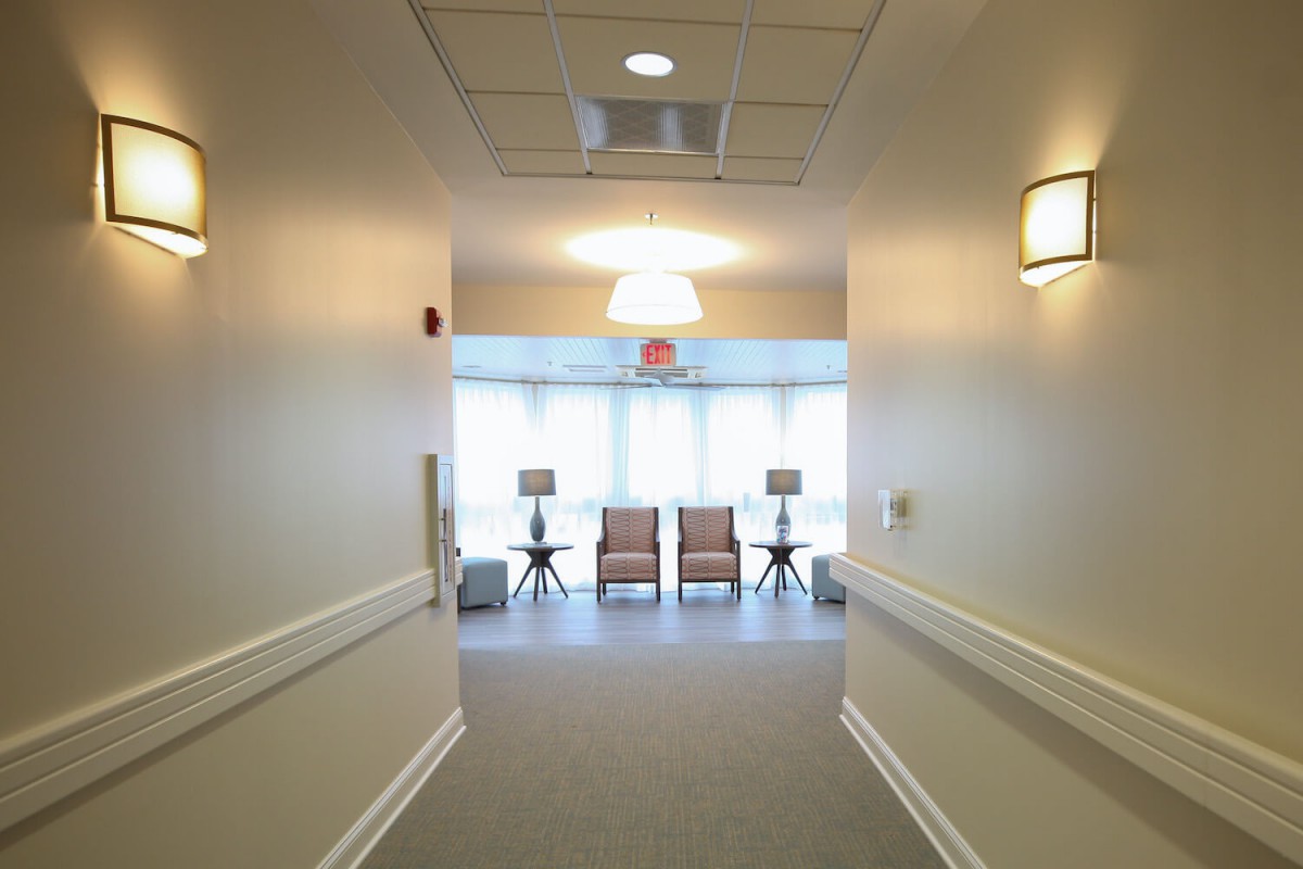 A well-lit hallway with chairs and windows at the end.