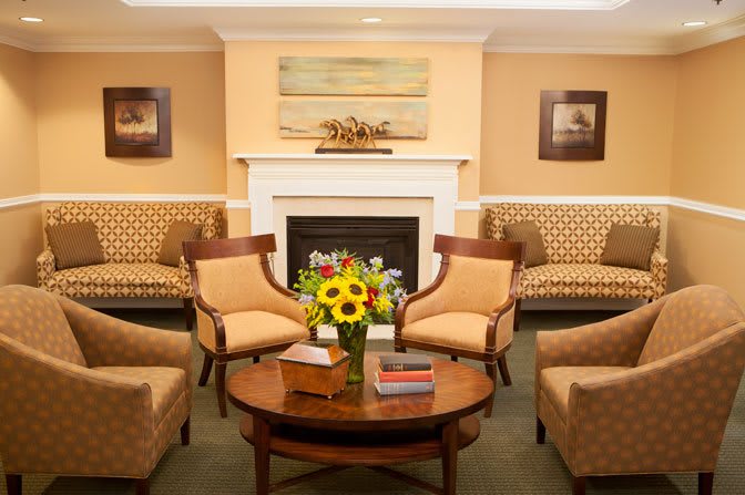 A cozy living room with comfortable chairs arranged around a central table and a fireplace, decorated with vibrant sunflowers.