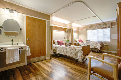 A spacious and well-lit patient room in a hospital, featuring two beds and modern furnishings.