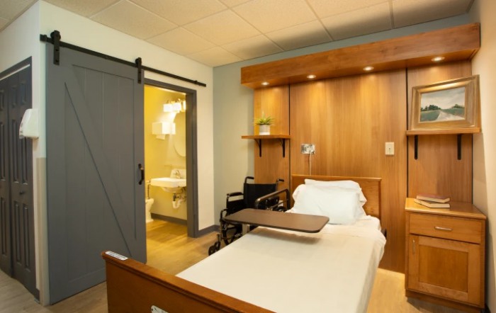 A modern hospital room featuring a patient bed and wheelchair, with an adjoining bathroom.
