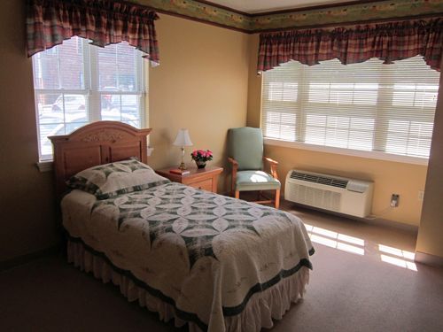 A cozy bedroom with a single bed, a chair by the window, and a small nightstand.