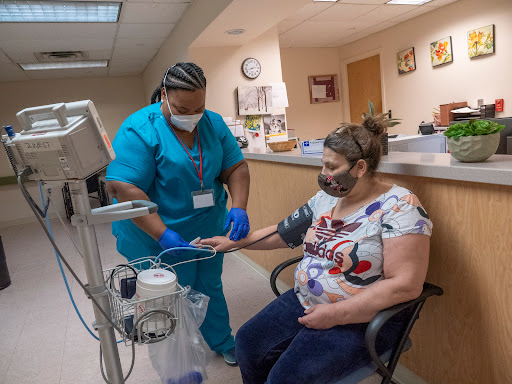 A nurse assists a patient with a blood pressure monitor in a clinic setting.