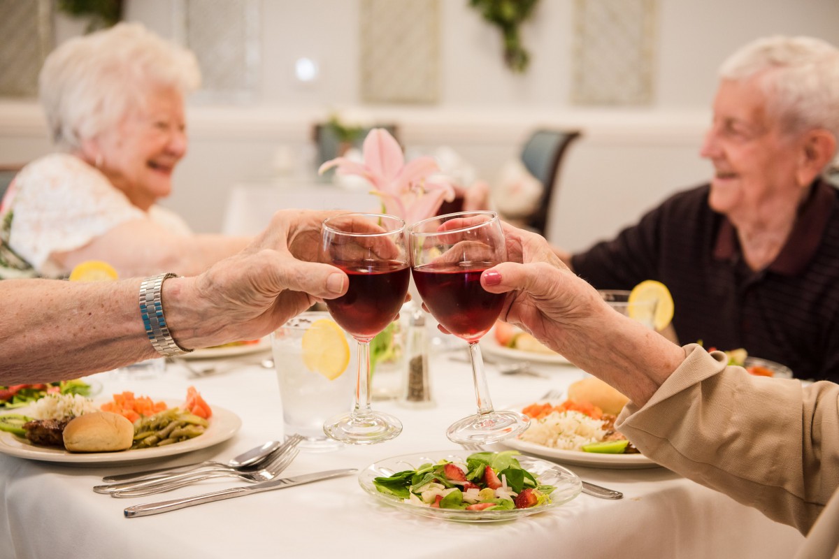 Elderly friends enjoying a dinner together and toasting with glasses of wine.