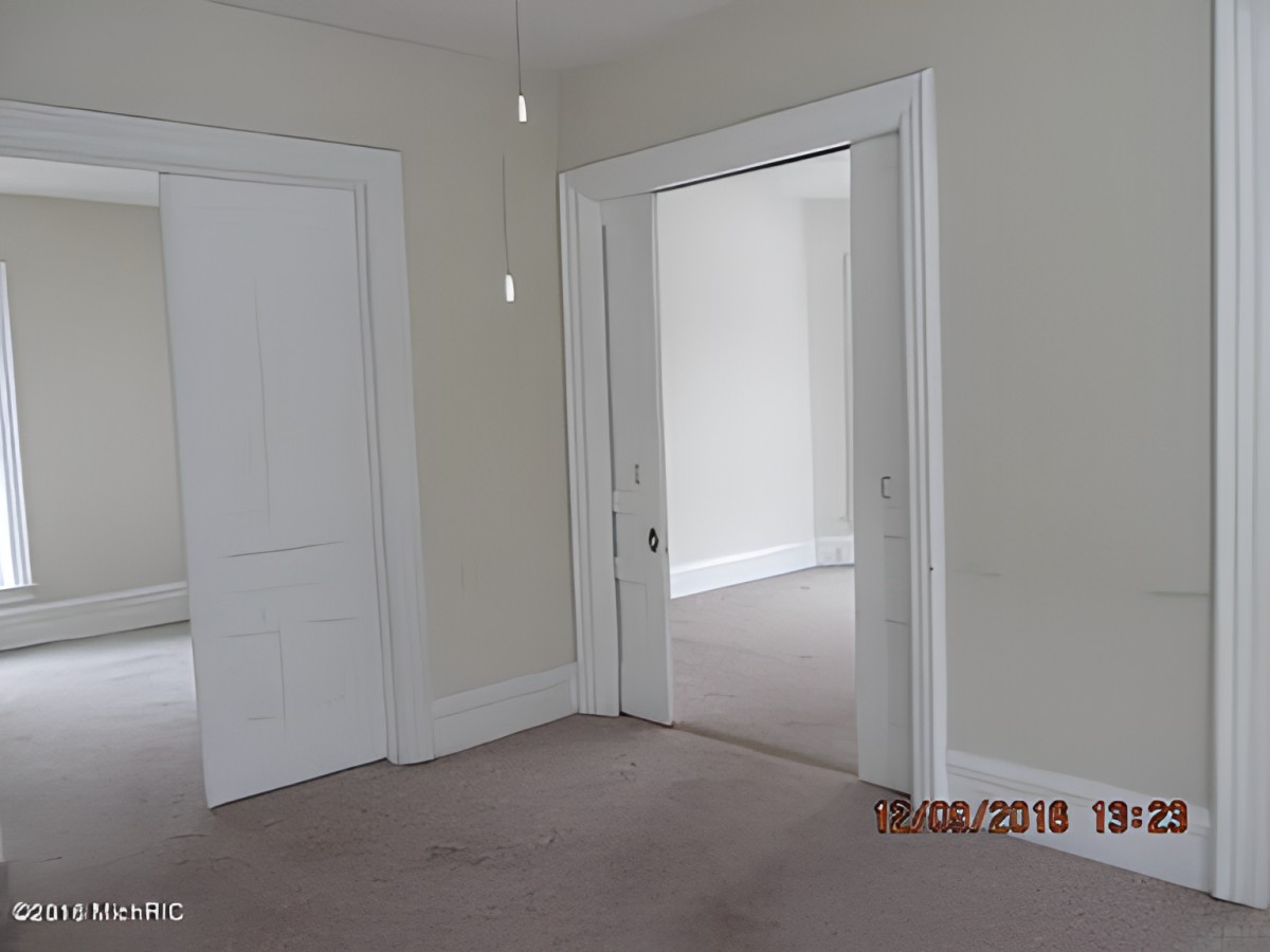 An empty room with carpet flooring, featuring neutral-colored walls and white trim around the doors.