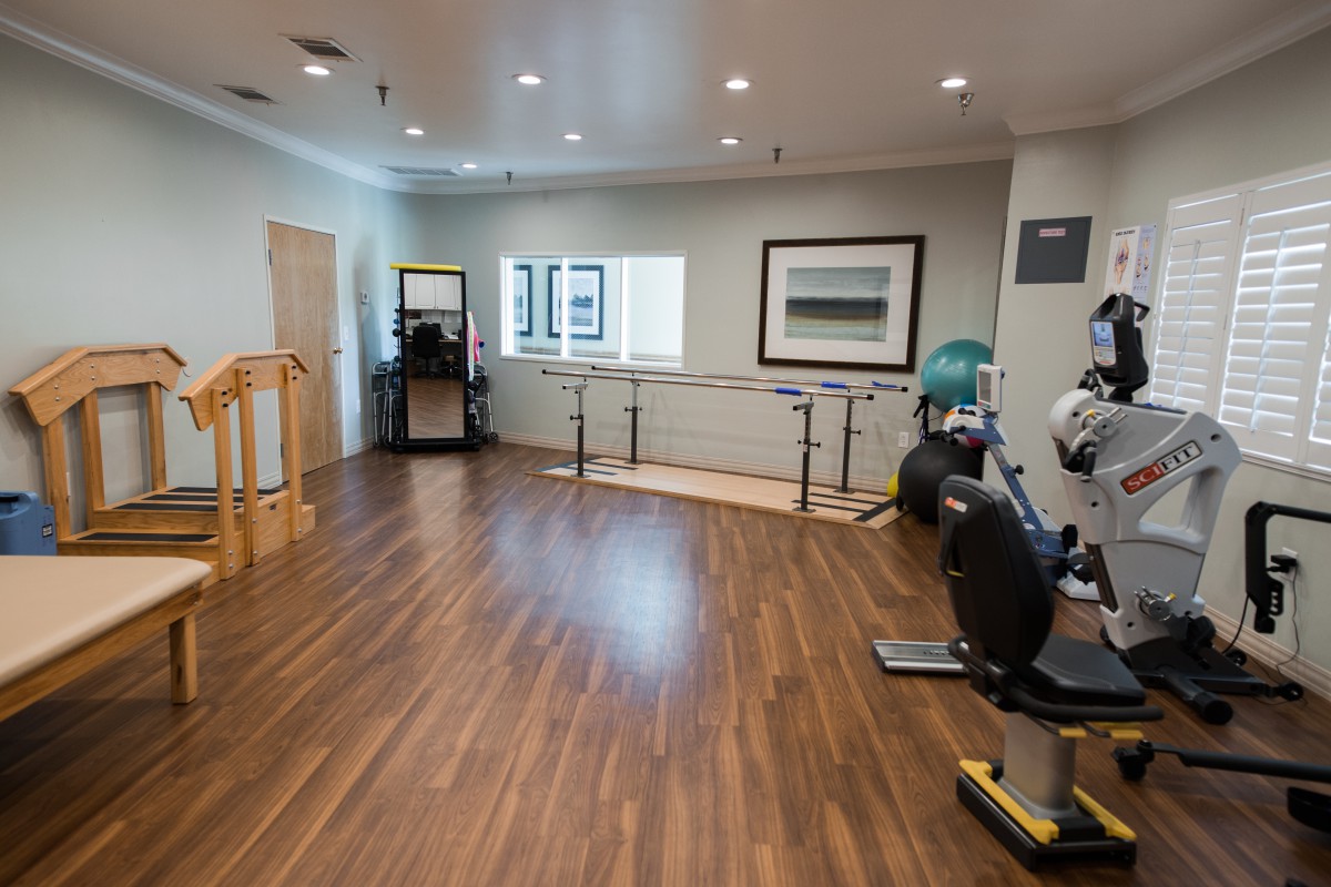 A spacious rehabilitation room equipped with exercise machines and parallel bars.