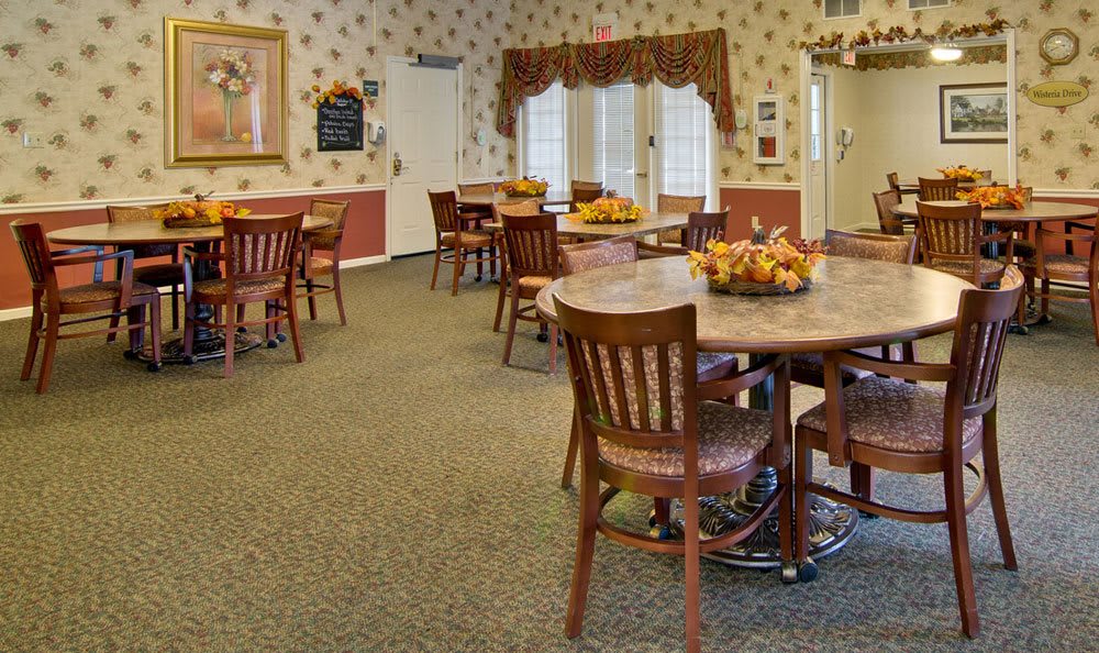 A cozy dining room with several tables and chairs, decorated with floral arrangements and warm colors.