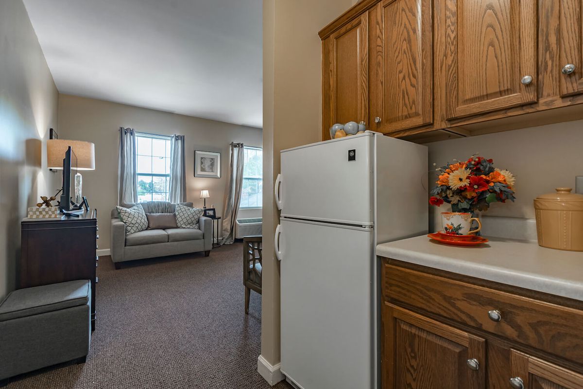 A cozy apartment interior featuring a kitchen with wooden cabinets and a refrigerator, leading into a comfortable living room with a couch.