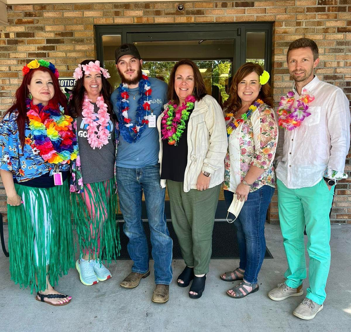 A group of people dressed in Hawaiian-themed attire, wearing colorful leis, at a themed event.