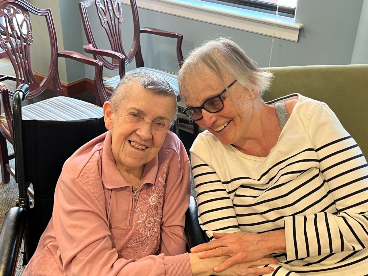 Two elderly individuals smiling and sitting together indoors.