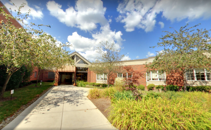 A school building with a landscaped entrance, under a partly cloudy sky.
