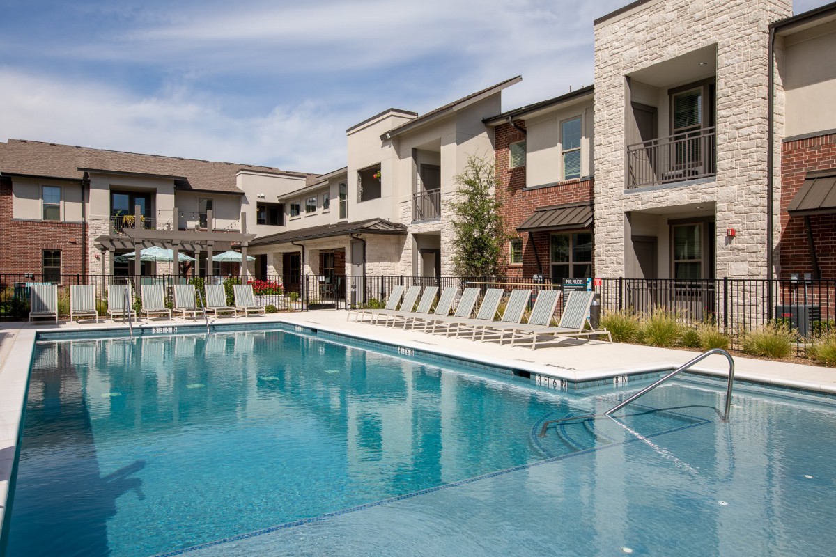 A modern apartment complex with a large outdoor swimming pool and lounge chairs.