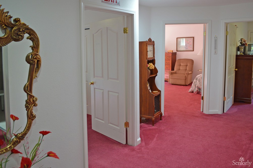 A hallway with pink carpet leading to rooms with doors slightly ajar.