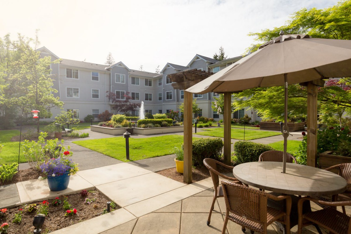 A peaceful garden patio with seating and a fountain in front of a residential building.
