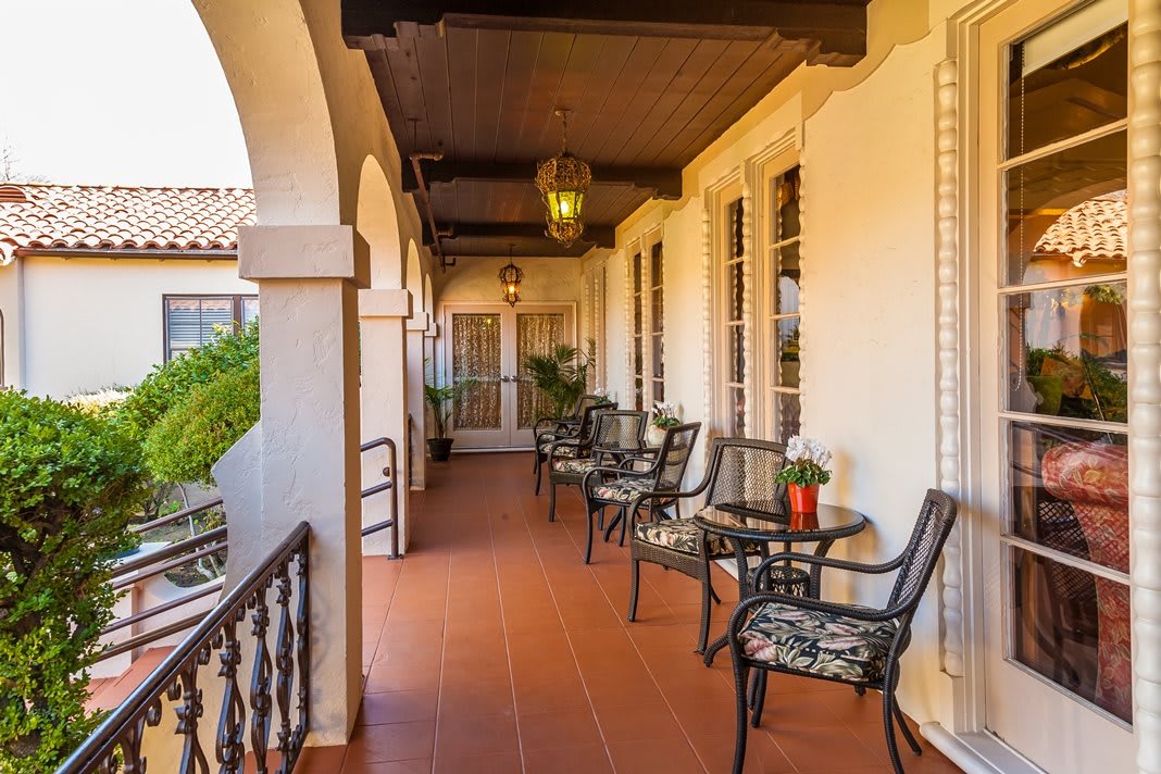 A charming veranda with arched architecture, featuring outdoor seating with tables and chairs, lit by a hanging lantern and decorated with potted plants.