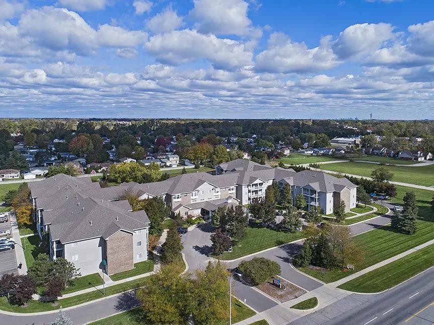 Aerial view of a residential area with buildings, roads, and green spaces under a cloudy sky.