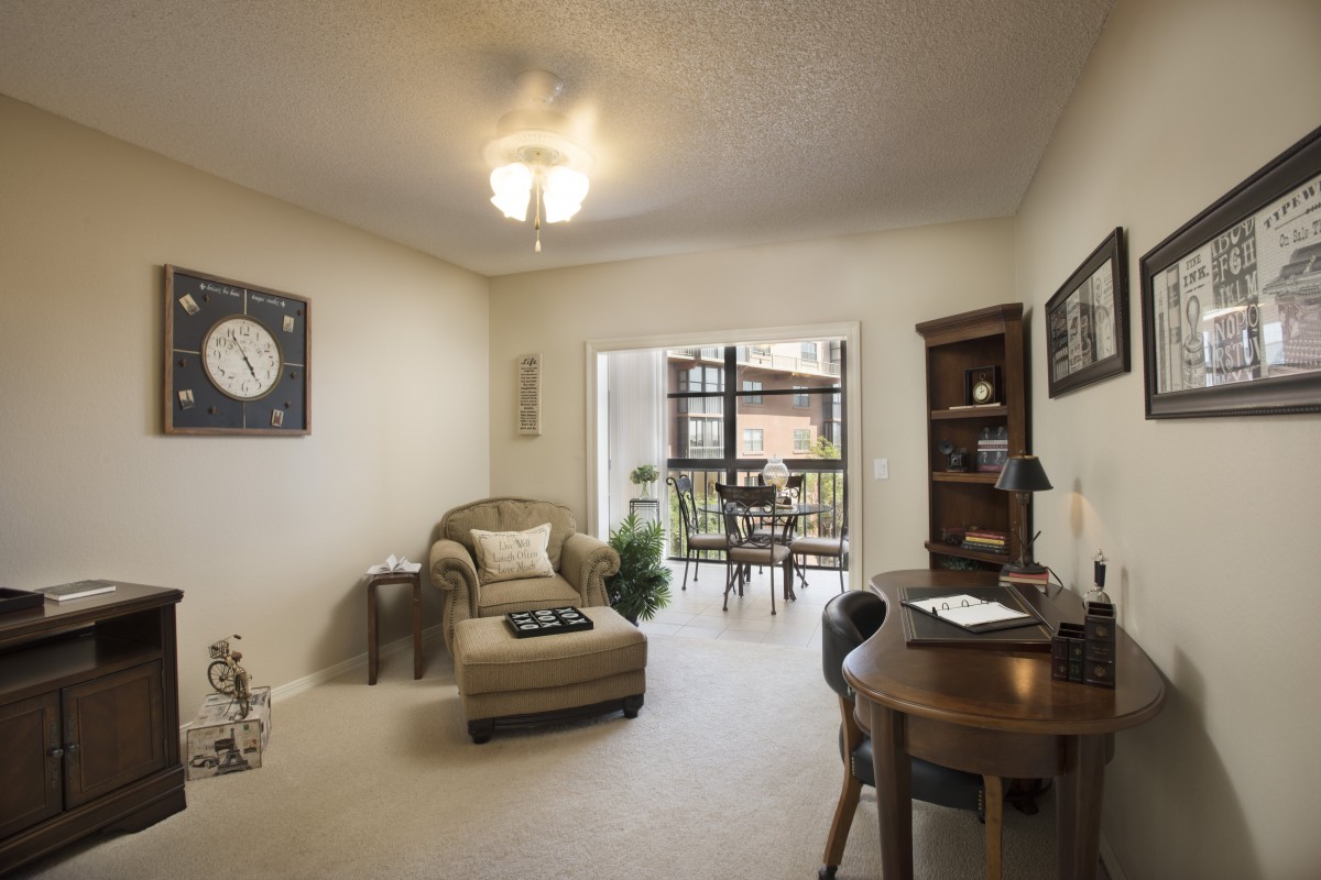 A cozy living space with a comfortable armchair, desk, and bookshelf, leading to an outdoor balcony.