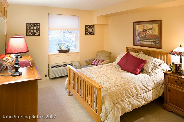 A cozy bedroom with a wooden bed frame, decorated with pillows and a quilted blanket, featuring a window allowing natural light.