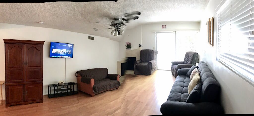 A spacious living room with a couch, armchair, fireplace, and a television mounted on the wall.