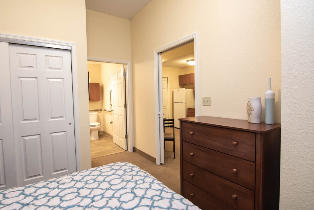A cozy bedroom featuring a dresser, bed, and an open doorway leading to a bathroom.