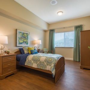 A cozy bedroom with a single bed, wooden furniture, and a large window with curtains.