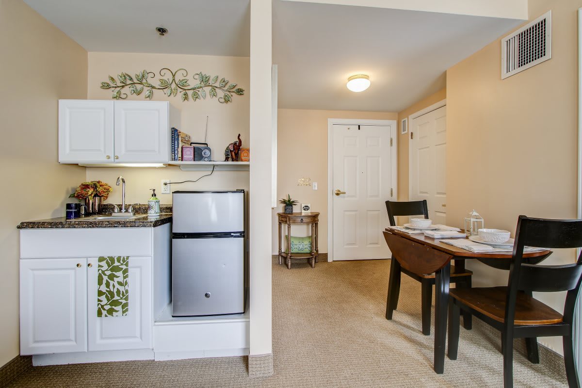 A cozy apartment interior featuring a small kitchen with white cabinets and a compact fridge, alongside a dining area with a neatly set table.
