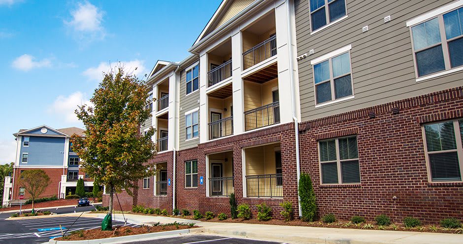 A modern apartment building with brick facades, balconies, and a nearby parking area.