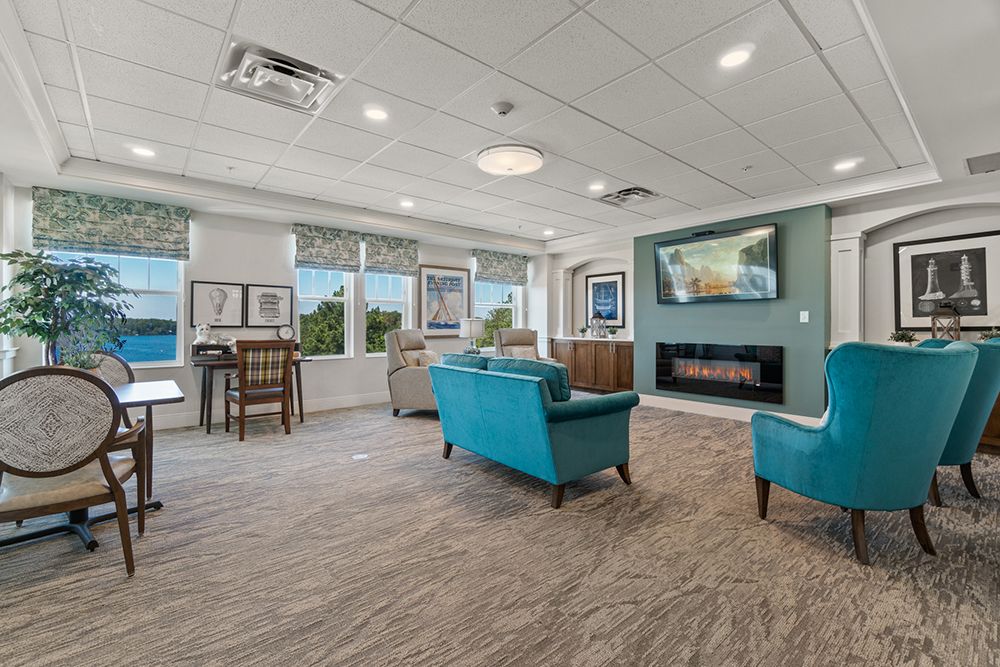 A modern lounge area featuring teal sofas, a wall-mounted television, and a fireplace against a backdrop of large windows.