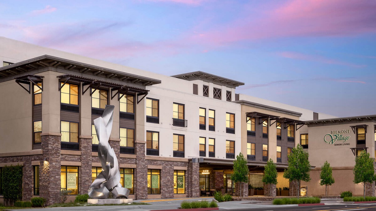 A modern apartment complex with a prominent sculpture in front, captured at sunset.