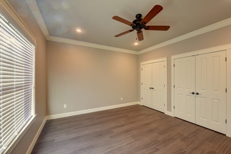An empty room with a ceiling fan and wood flooring, featuring neutral-colored walls and double closet doors.