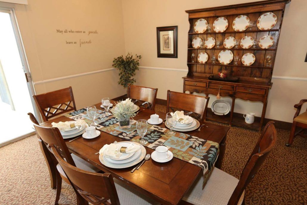 A neatly arranged dining room table with elegant dinnerware and a floral centerpiece.