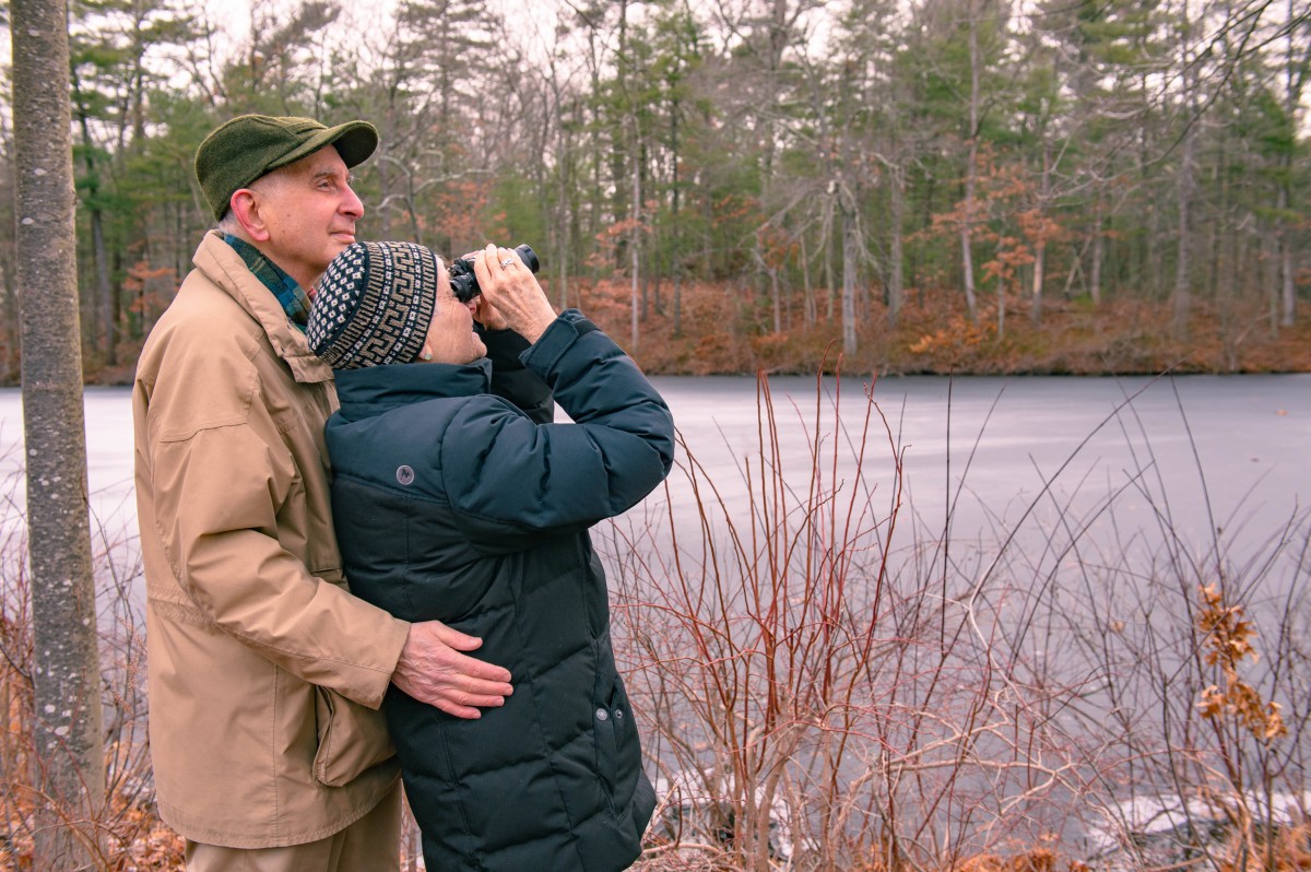 A couple birdwatching near a frozen lake in winter.
