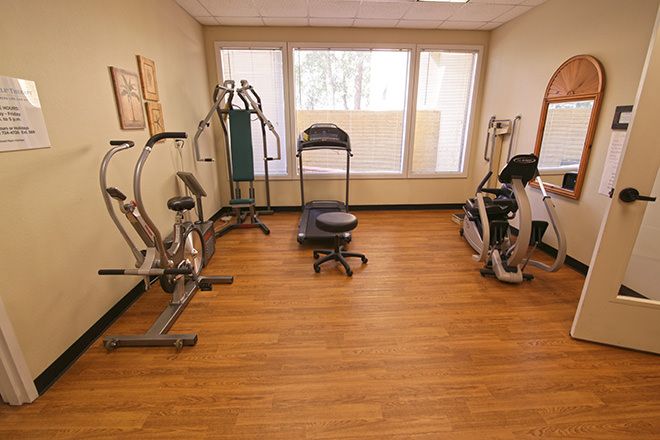 A small indoor gym with various exercise machines and wooden flooring.
