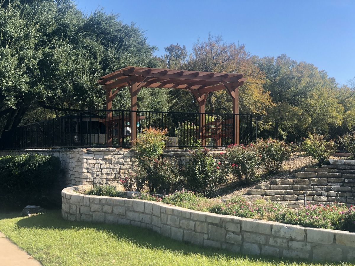 A scenic outdoor garden area featuring a pergola and landscaped stone walls.