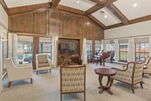 A spacious living room featuring a vaulted ceiling, wood paneling, and elegant furniture with ample natural light from large windows.