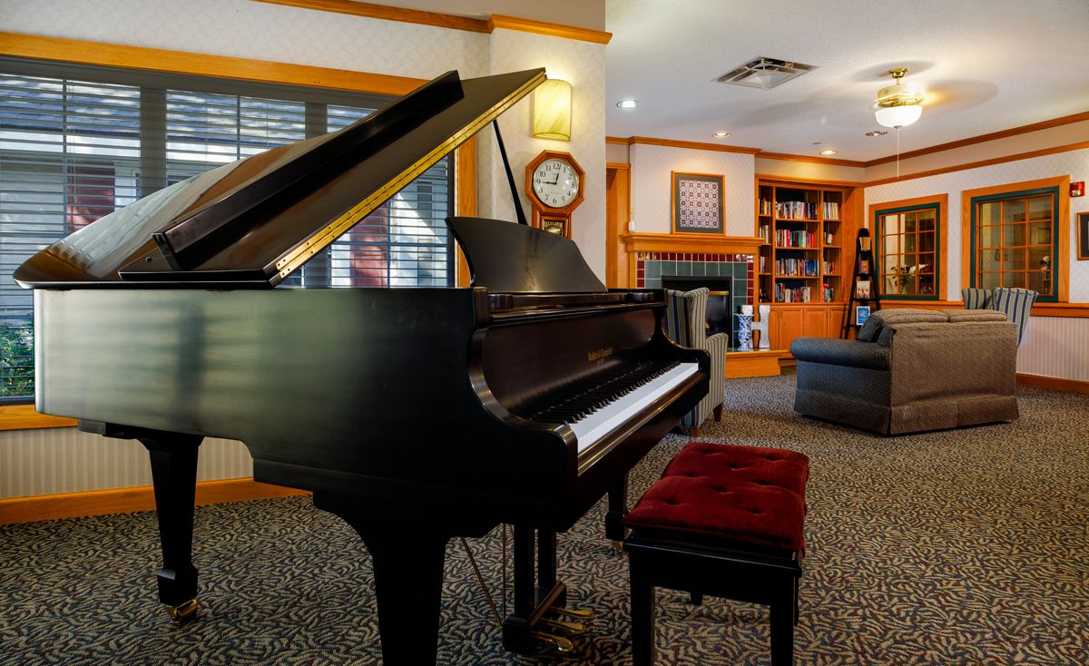 A cozy music room with a grand piano, surrounded by bookshelves and comfortable seating.