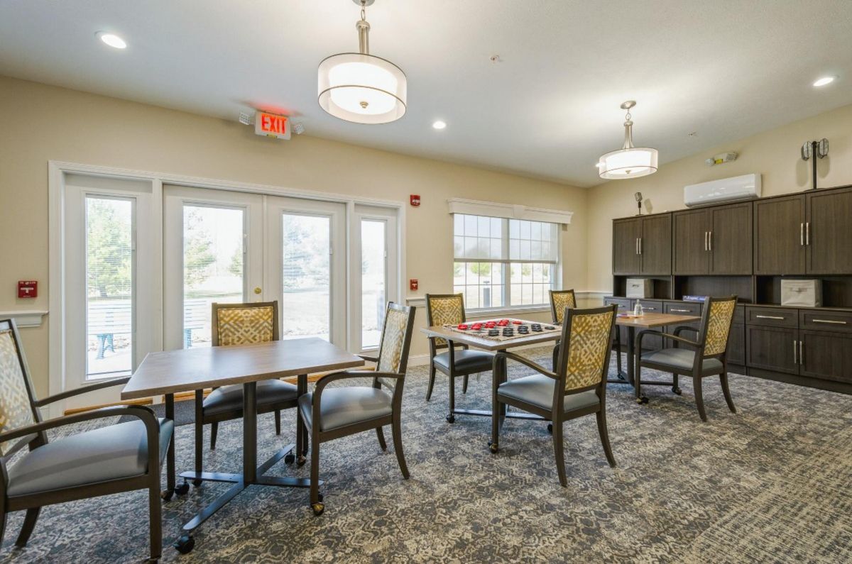 Bright dining area with tables and chairs, illuminated by overhead lighting and natural light from large windows.