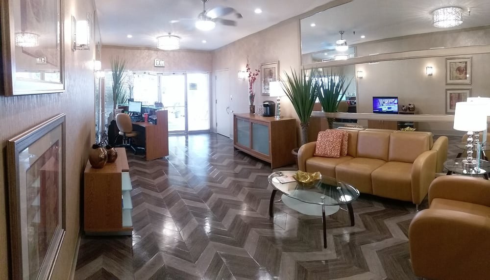 A modern office waiting room with a reception desk, sofa seating, and indoor plants.