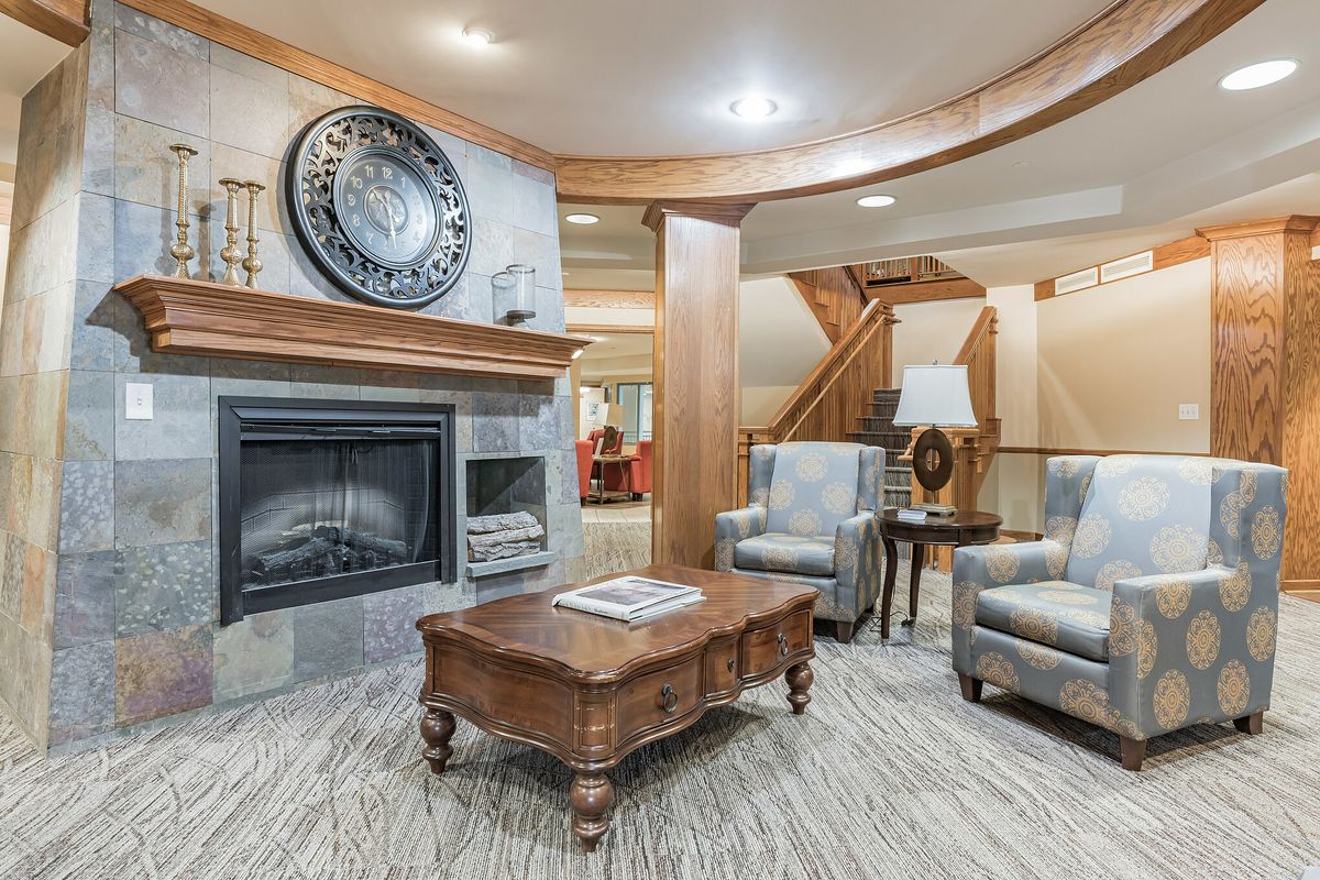 A cozy living room featuring a fireplace, two armchairs, and a wooden coffee table.