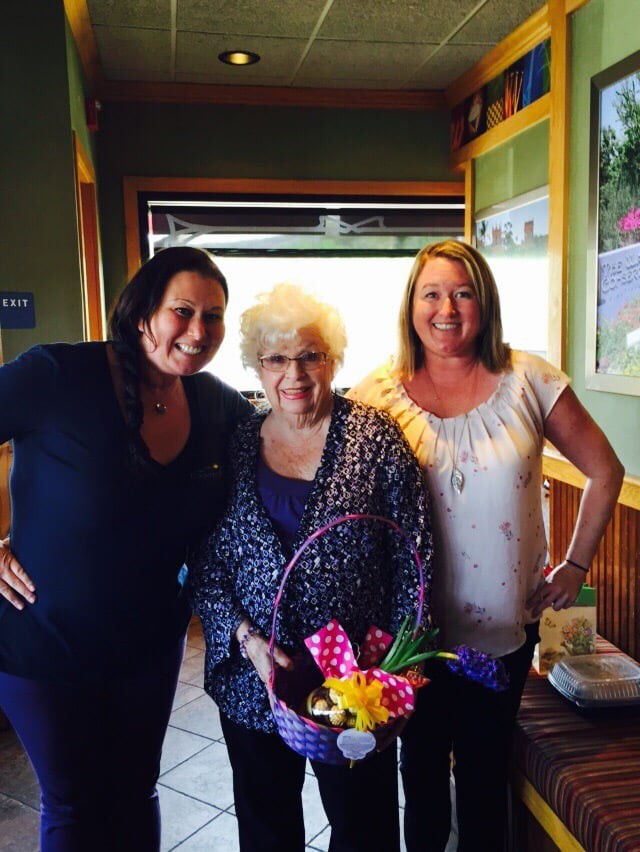 Three women posing together indoors, holding a bouquet of flowers.