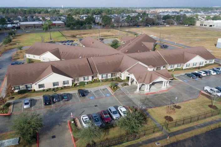 Aerial view of a large building with a parking lot and surrounding landscaping in a suburban area.