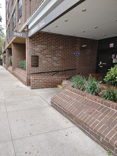 A view of a brick building entrance with landscaped greenery along the sidewalk.