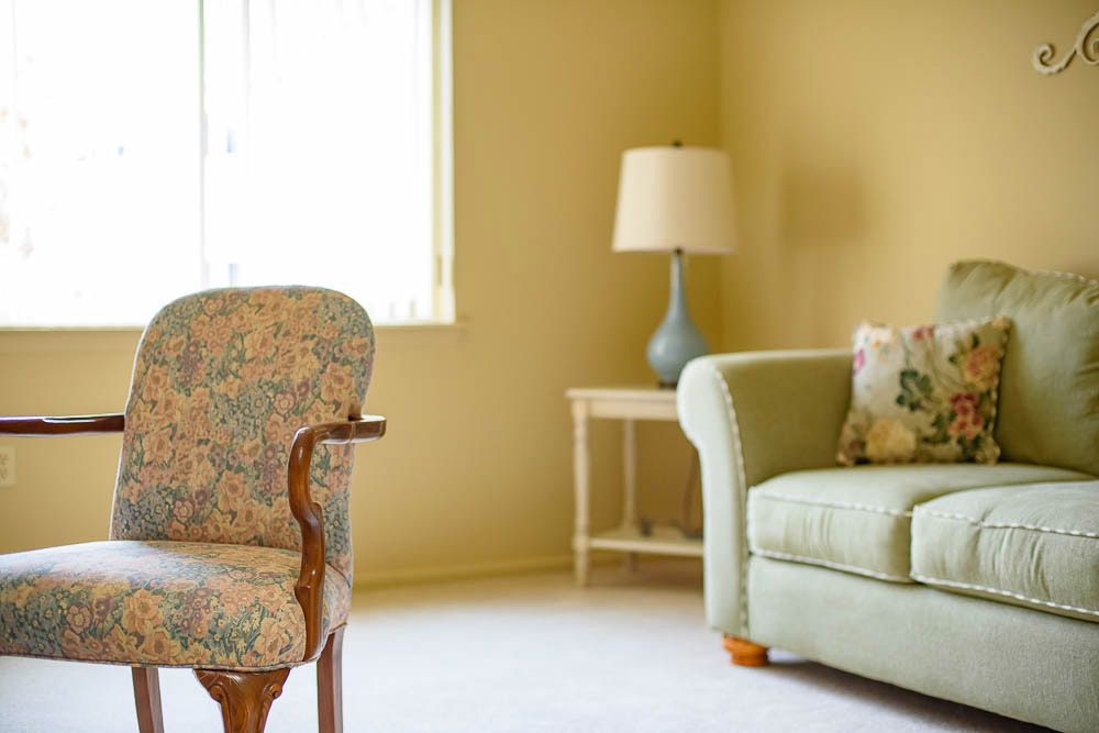 A cozy living room with a sofa, lamp, and floral chair by the window.