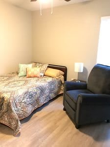 A cozy bedroom with a bed, armchair, and lamp.