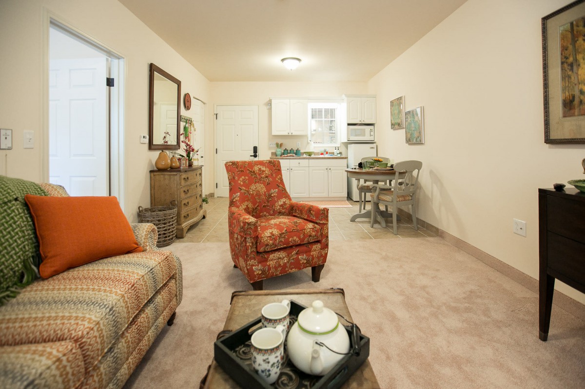 A cozy living room with an armchair, sofa, and a view into the kitchen area.