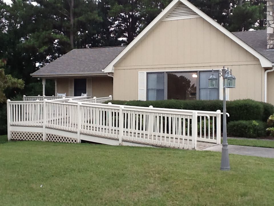 A residential house with a wheelchair-accessible ramp leading to the porch, surrounded by greenery.